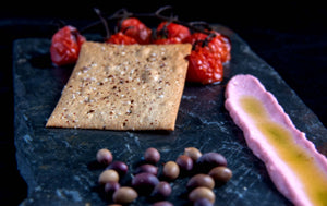 Lavosh sourdough cracker on black plate and black background with locally grown cherry tomatoes and a smear of dip. 